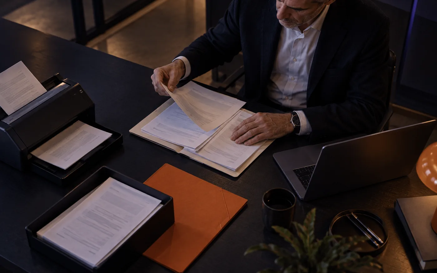 Profesional revisando documentación y carpetas en su escritorio, con el portátil abierto